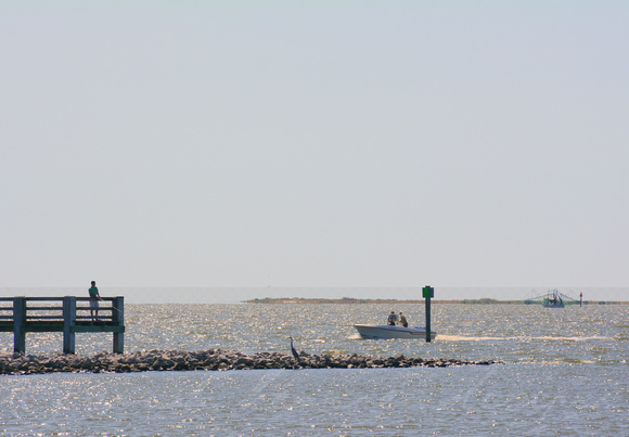 A man fishes & a heron lingers as the pleasure boat heads into the OS Harbor