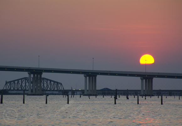 A cue ball sun sets over the Biloxi/OS bridge